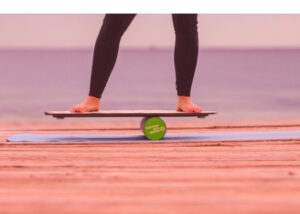 Woman's feet pictured on a beach while she keeps her balance on board placed on cylinder